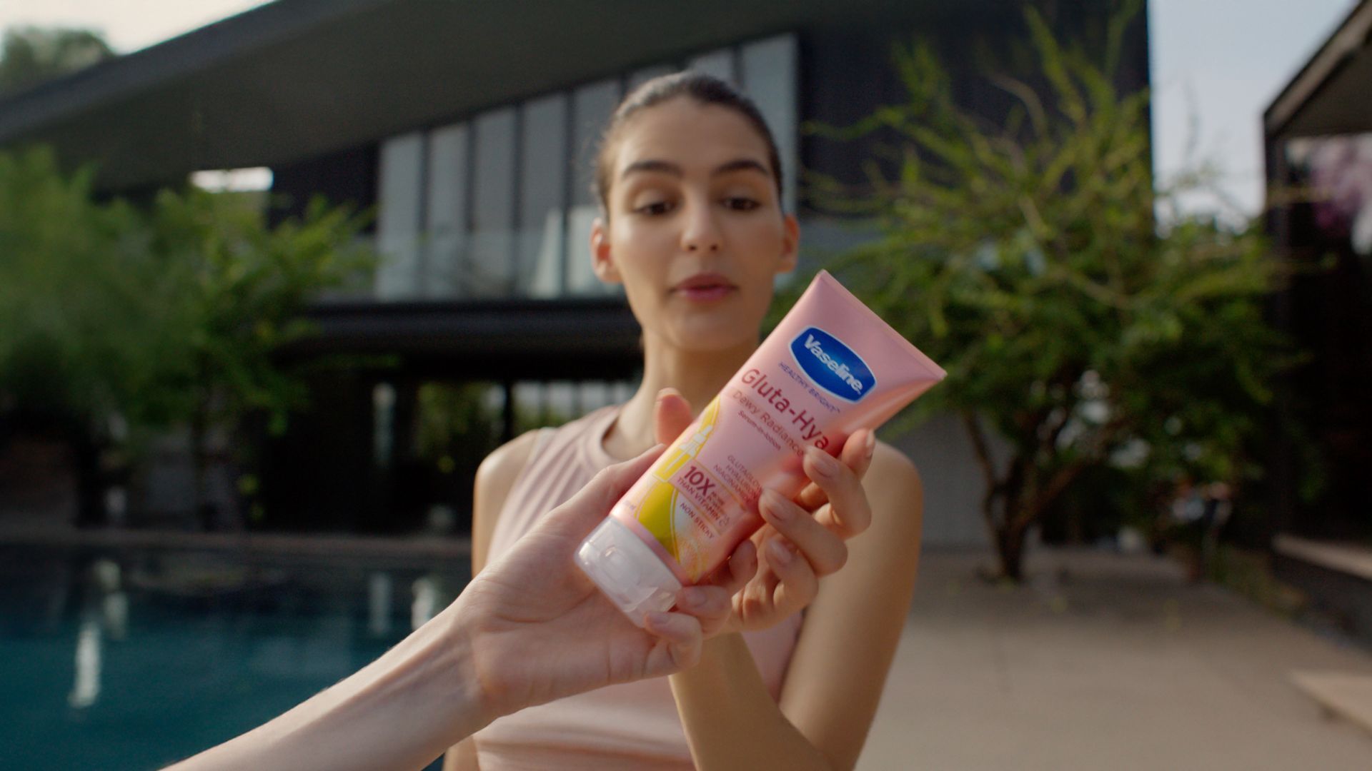 Woman holding a pink Vaseline Gluta-Hya lotion tube outdoors.