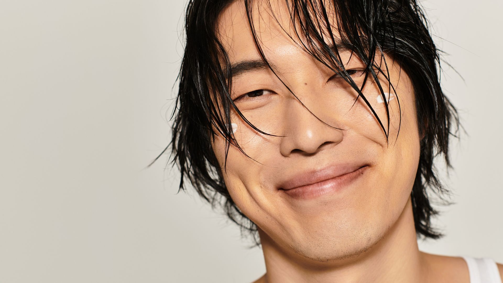 Man with wet hair smiling, cream dots on cheeks.