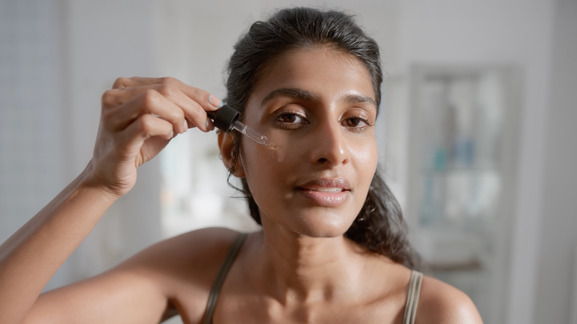 Woman applying serum with dropper to her face.