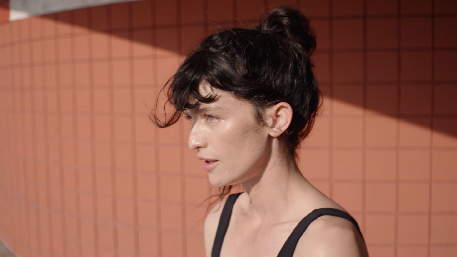 Profile of a woman with hair in a bun against a tiled orange wall.