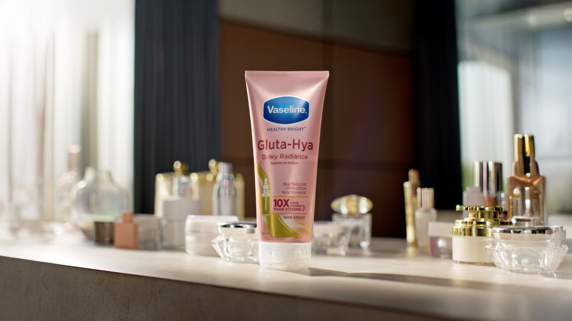 A tube of Vaseline's Gluta-Hya Dewy Radiance serum-in-lotion displayed among various skincare products on a countertop.