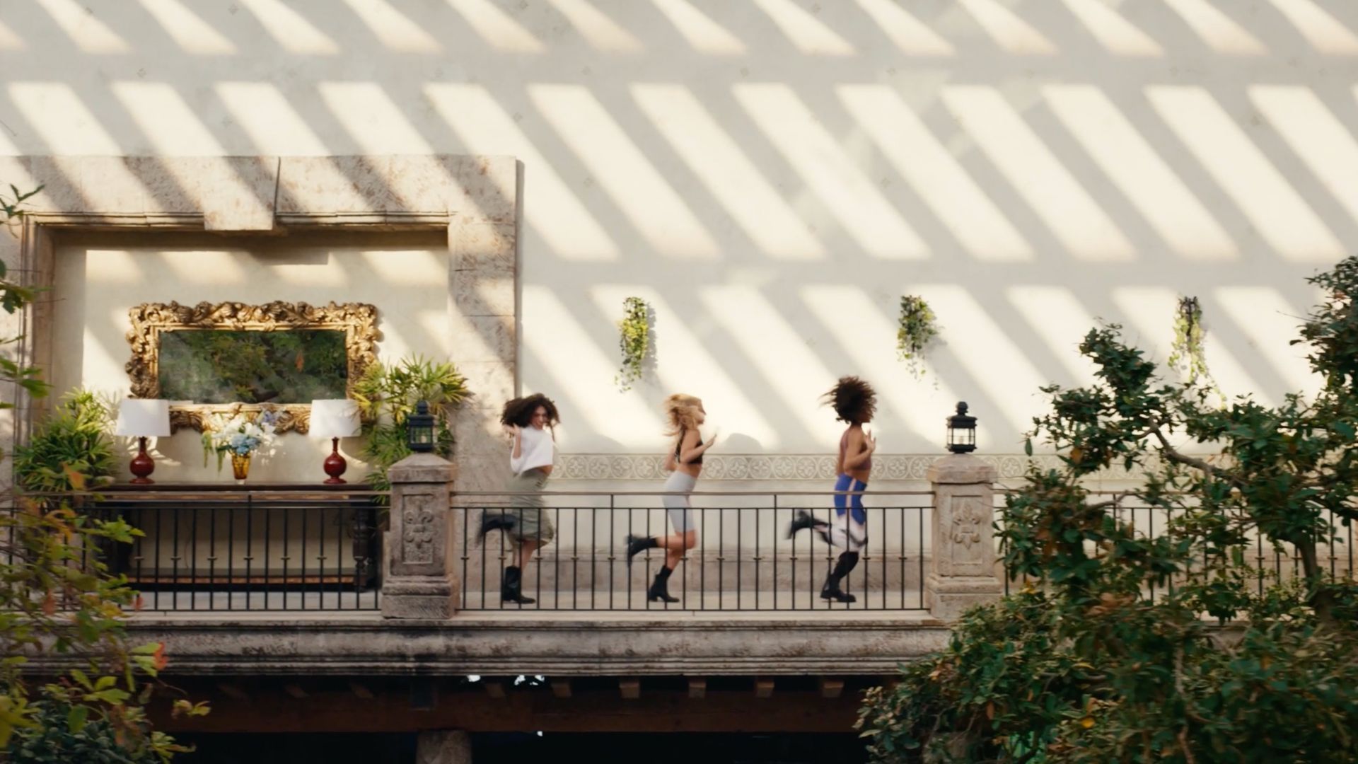 Three people dancing on a sunny balcony with plants and artwork.