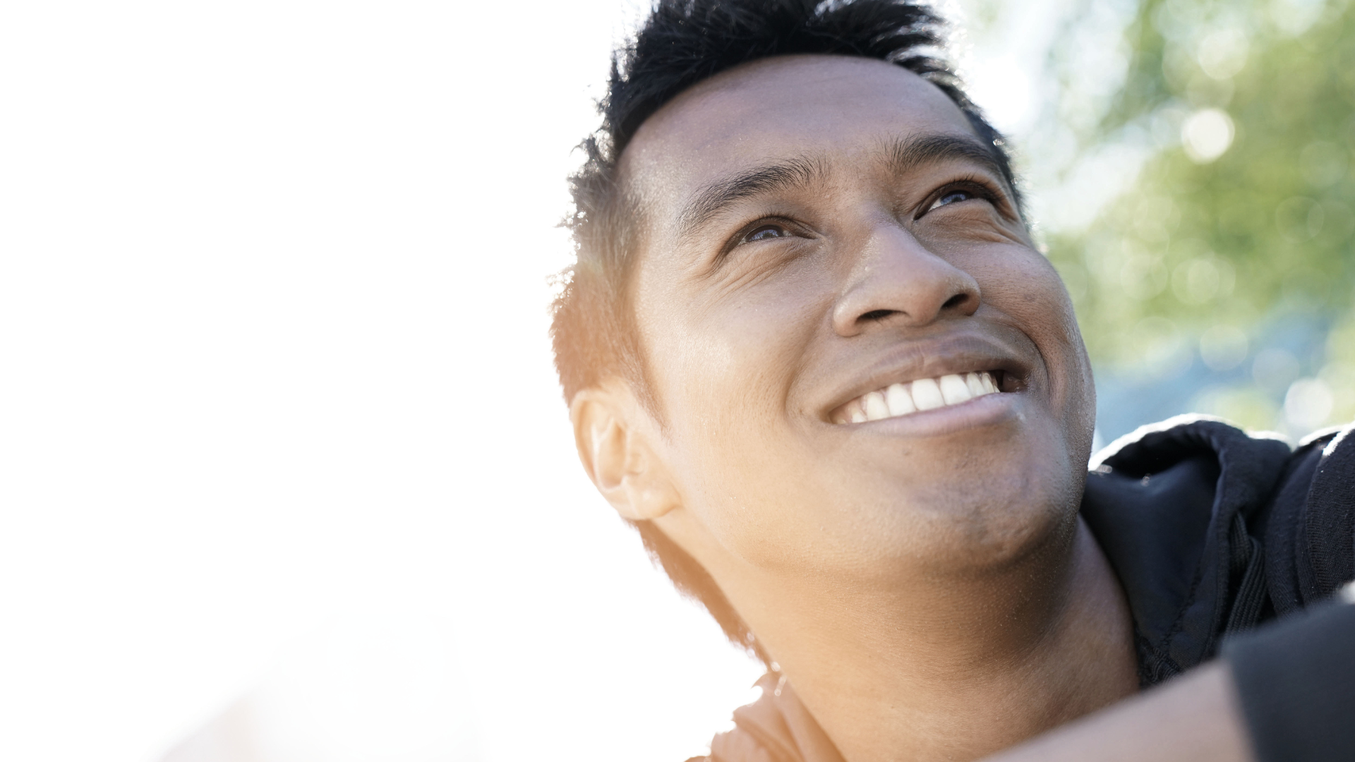 Man smiling and looking upwards in sunlight.