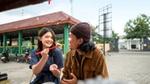 Two people at an outdoor cafe, one offers food with chopsticks, both smiling.
