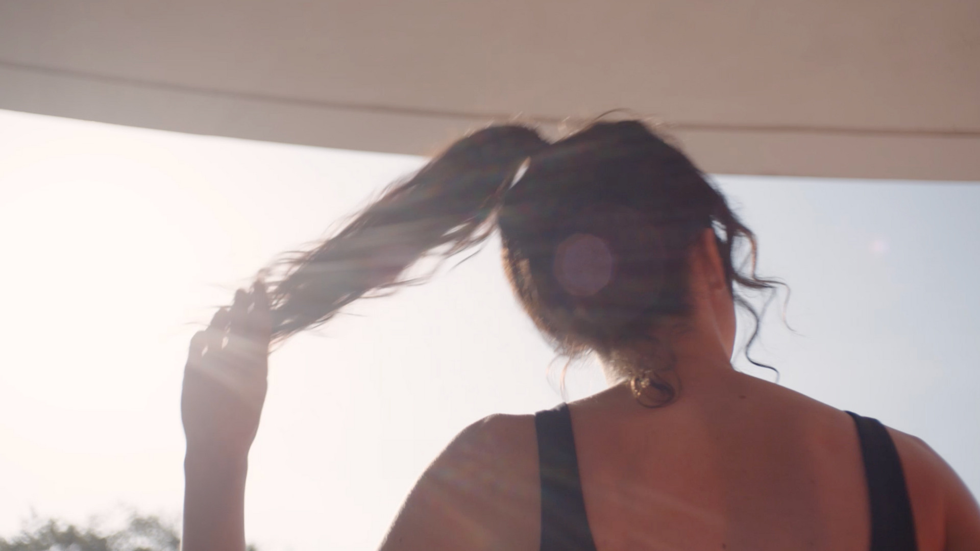 Person in sunlight holding ponytail, viewed from behind.
