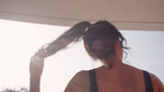 Person in sunlight holding ponytail, viewed from behind.