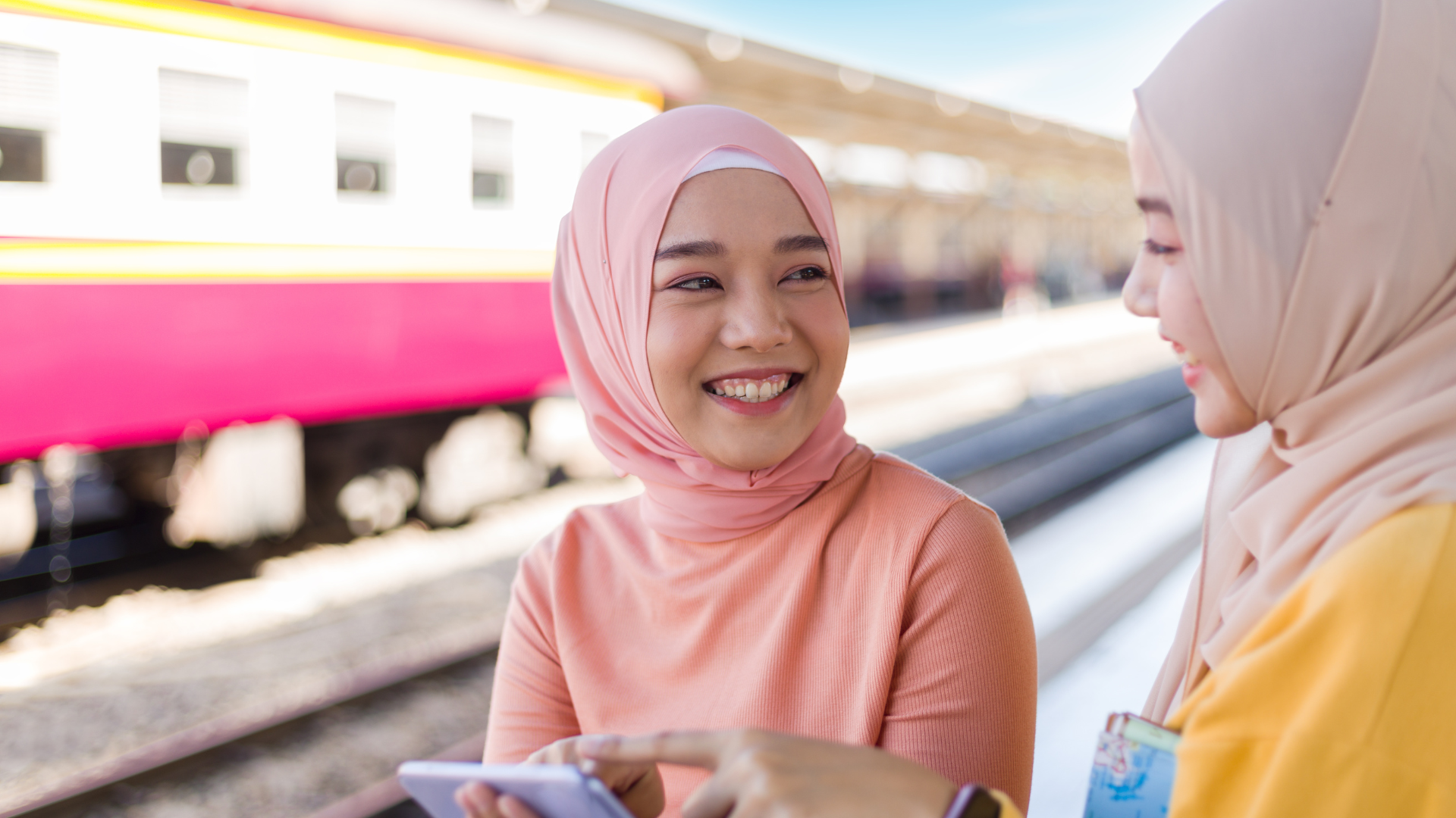 Two women smiling at a train station.