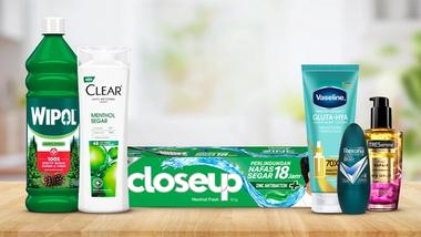 A variety of products on a wooden surface, including cleaning solution, shampoo, lotion, toothpaste, deodorant, and hair oil.