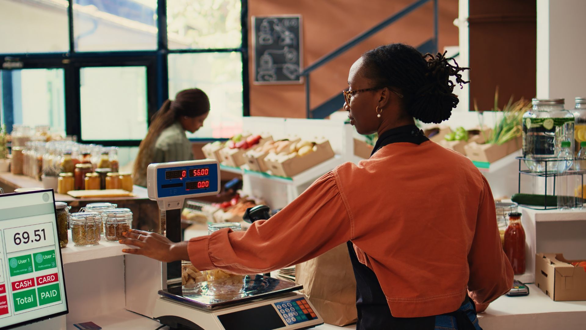 Shopkeeper weighing items on a digital scale in a grocery store.