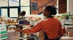 Shopkeeper weighing items on a digital scale in a grocery store.