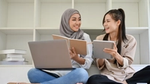 Two women smiling while studying with a laptop and notebook.
