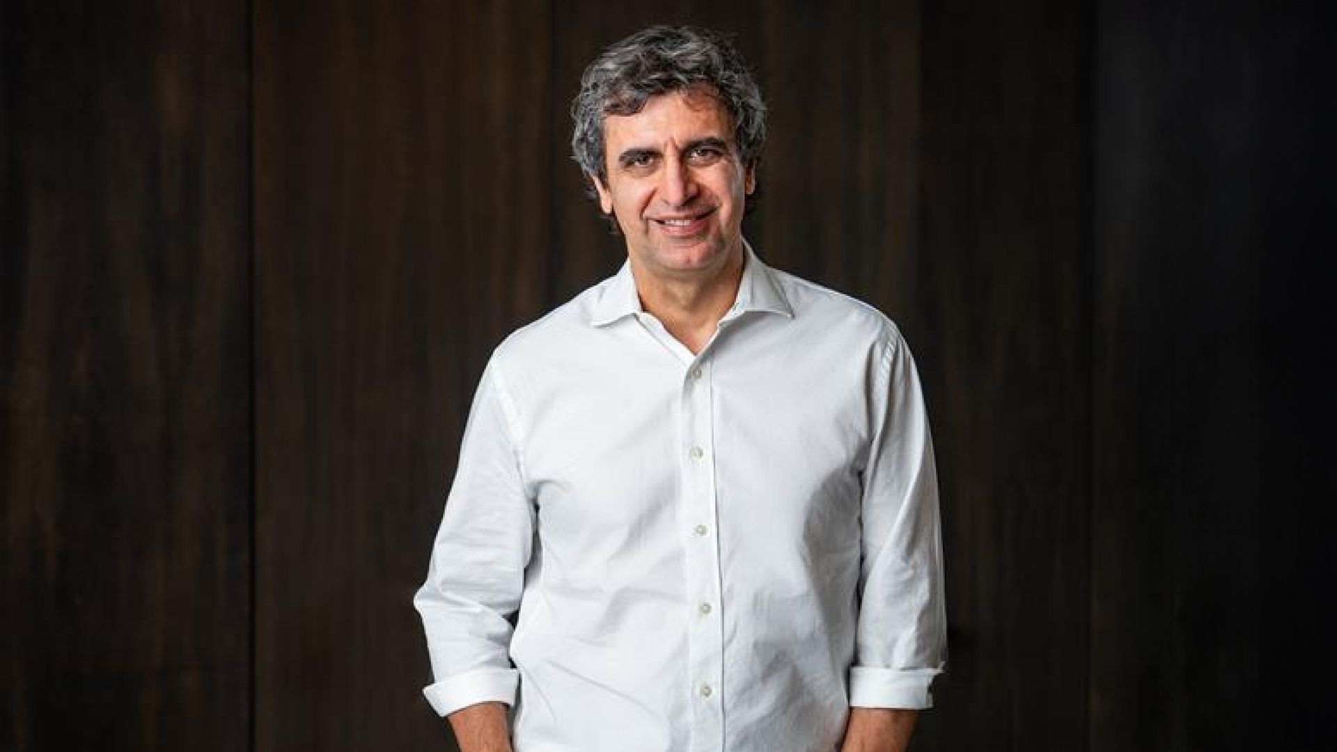 Fernando Fernandez in a white shirt standing against a dark wooden background