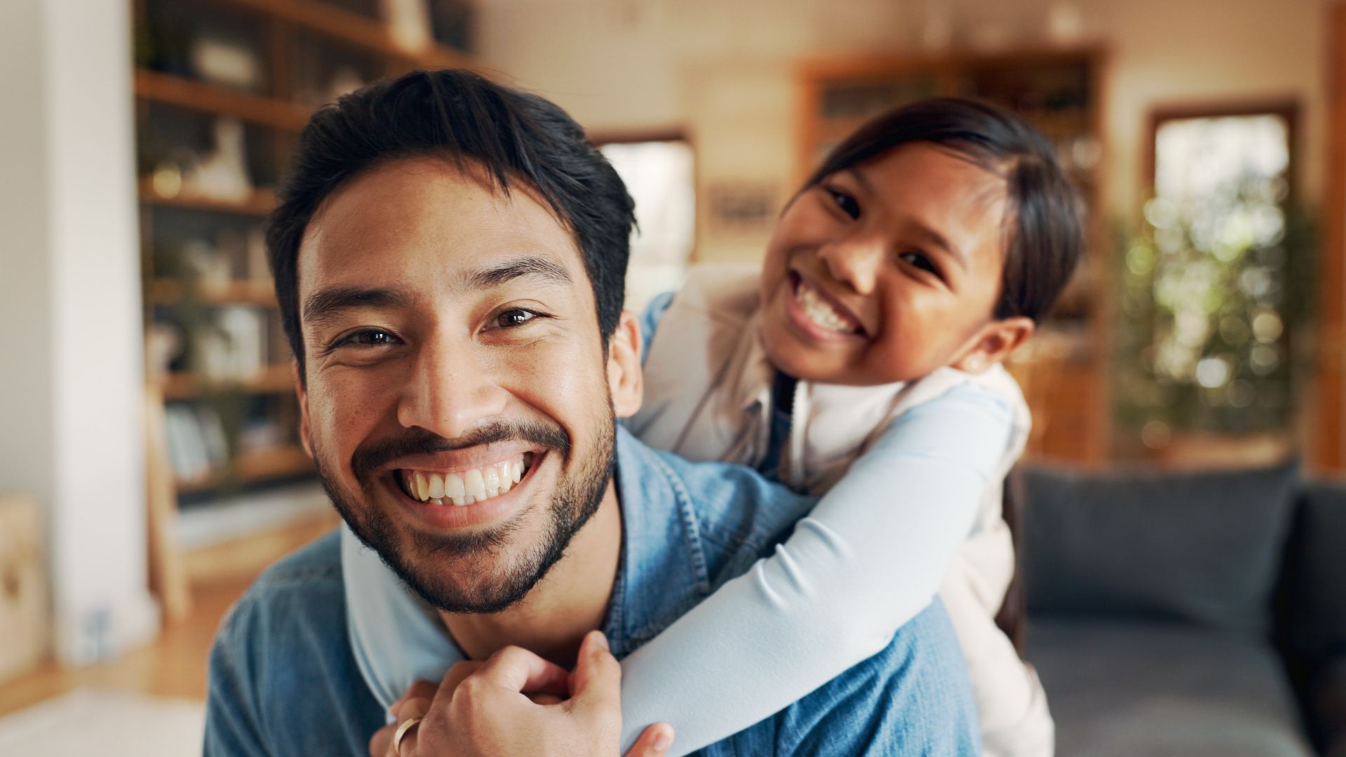 Smiling man with child on his back indoors.