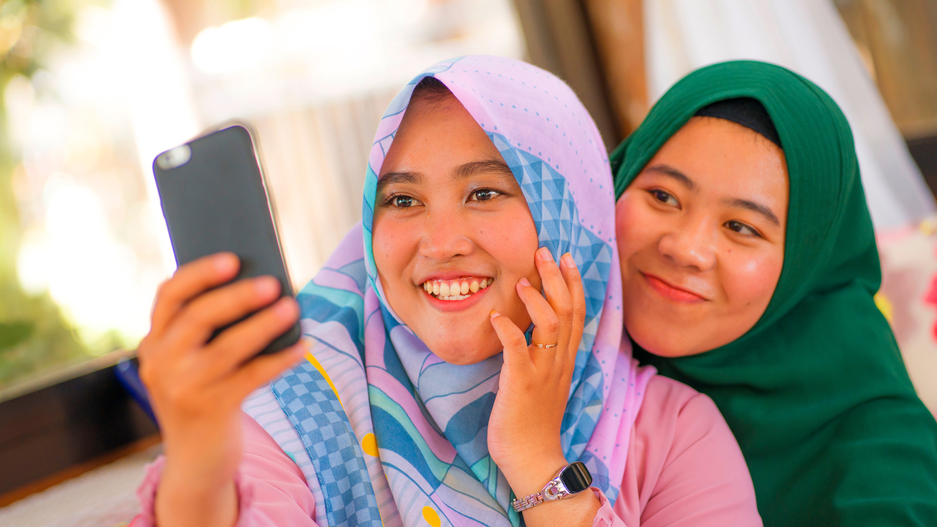 Two women in hijabs smiling while taking a selfie.