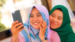 Two women in hijabs smiling while taking a selfie.